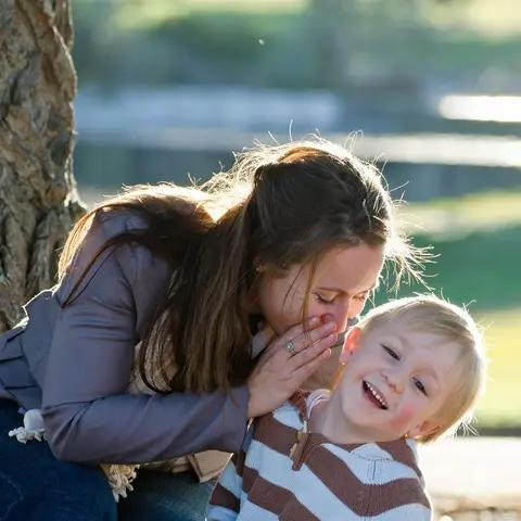 Mother whispering to her laughing young son outdoors
